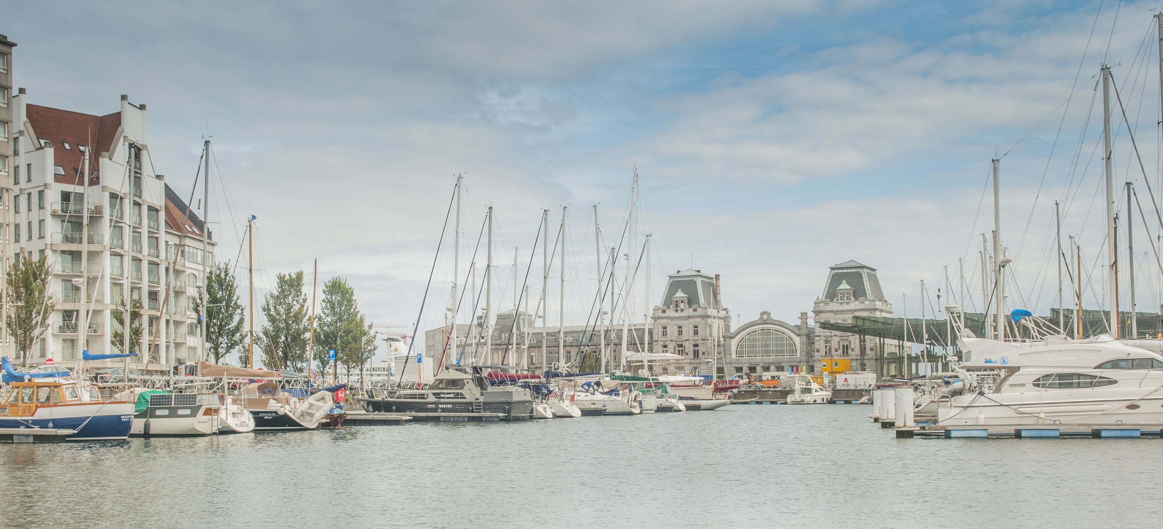 A marina with various boats docked, a large building with a distinctive tower, and a clear sky.