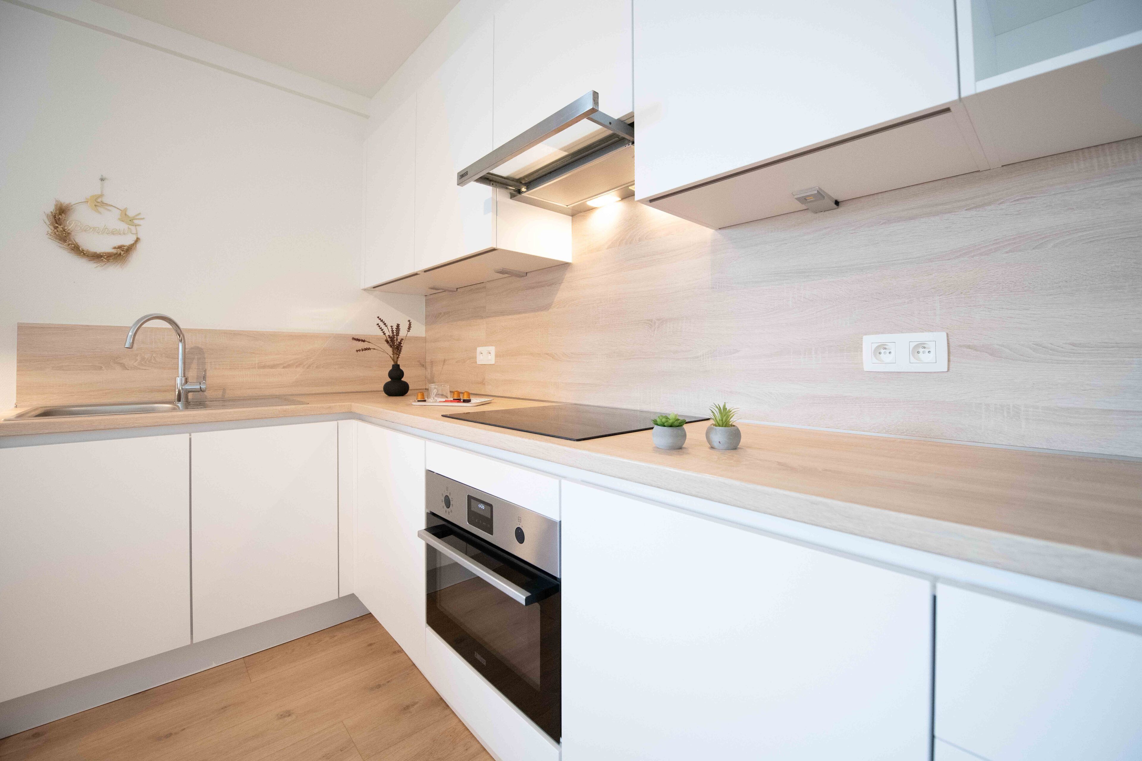 A modern kitchen with white cabinetry, a stainless steel sink, and a built-in oven.