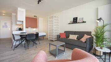 A modern living room with a grey sofa, a small coffee table, and a dining area with a table and chairs.