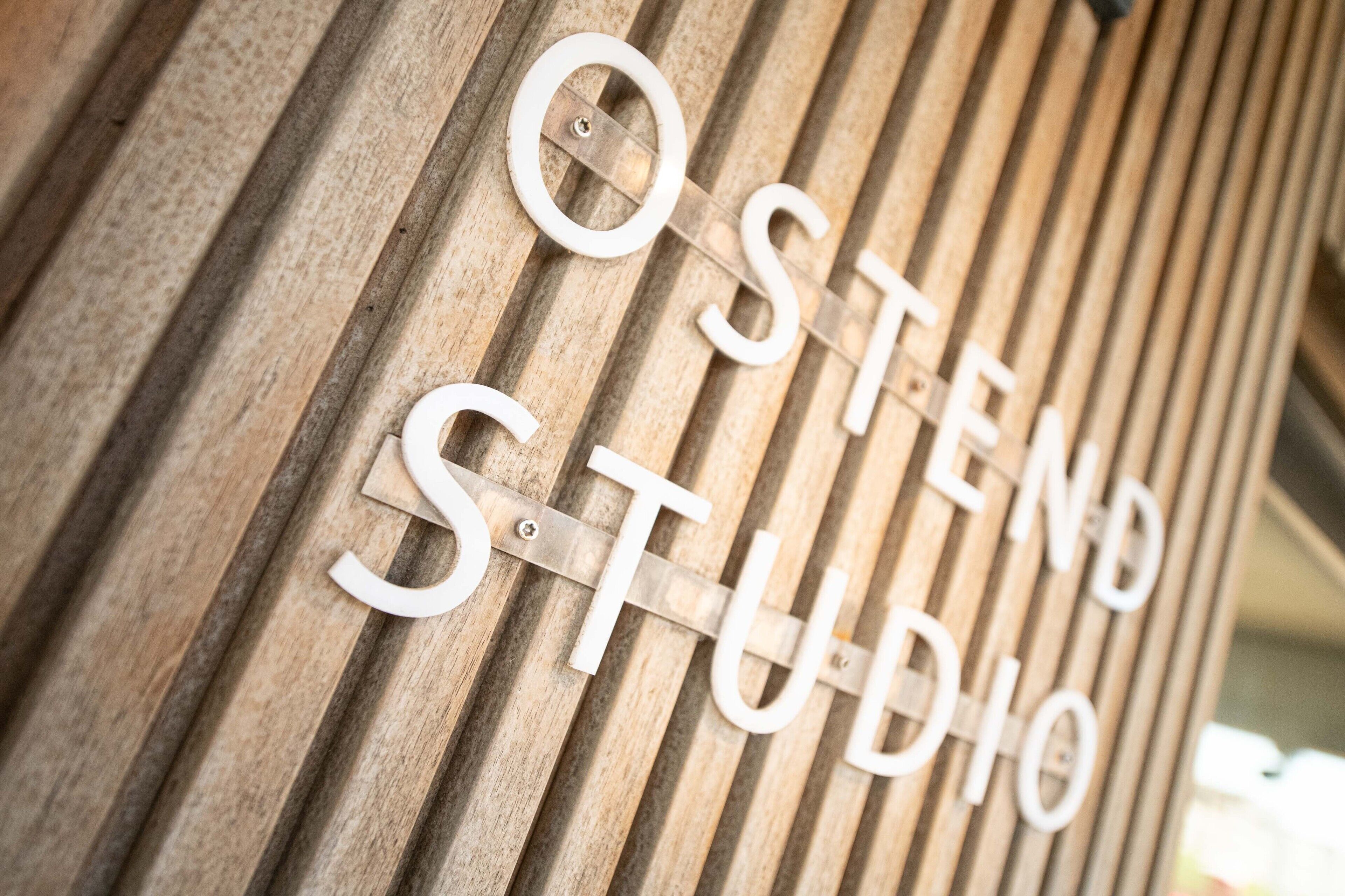 Un letrero de madera con el texto 'OSTEND STUDIO' sujeto a una pared de listones.