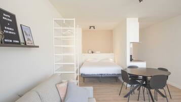 Ein modernes Hotelzimmer mit Bett, Esstisch mit Stühlen, Sofa, Kleiderschrank und einer Wandablage mit gerahmten Bildern.
