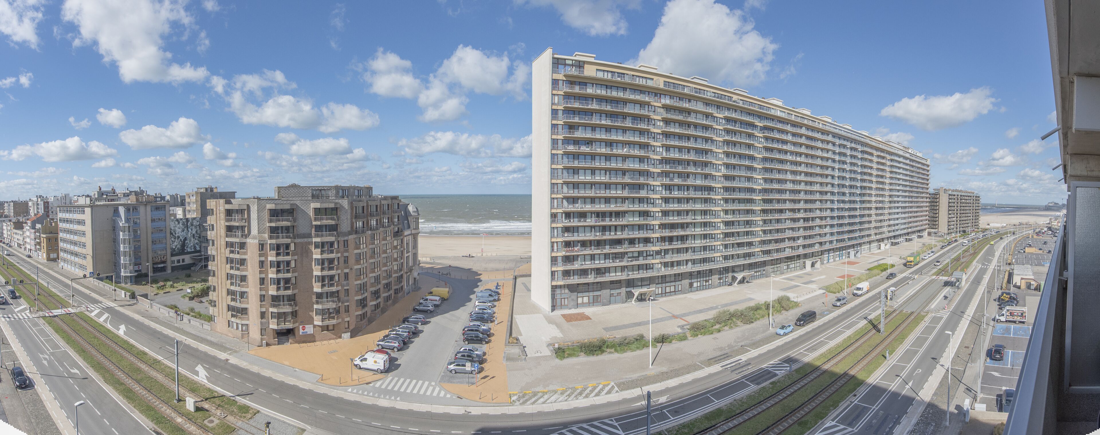 A high-rise hotel with a curved facade overlooking a beach and a busy road.