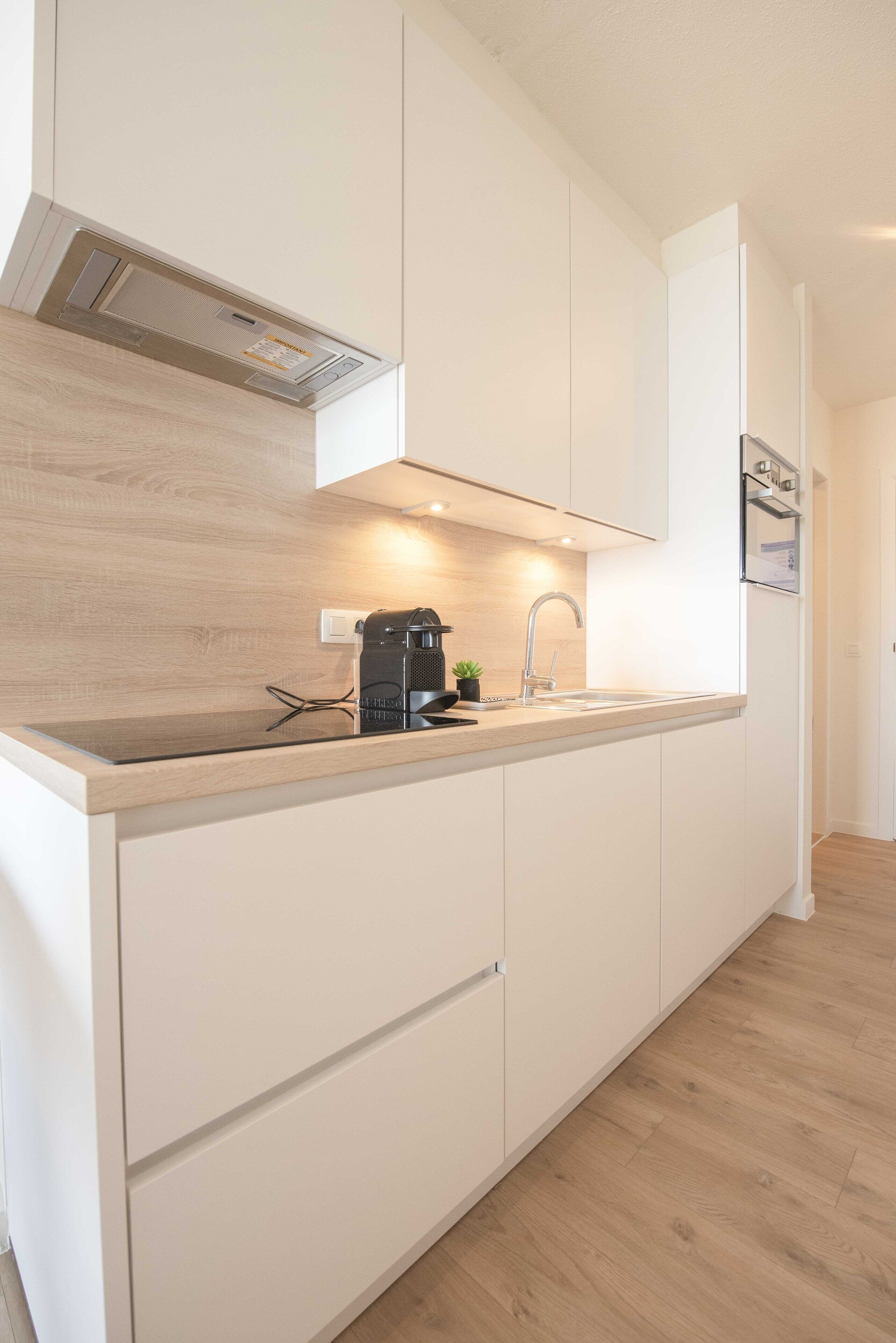 A modern kitchen with white cabinetry, a wooden countertop, a built-in stove, and a sink with a faucet.