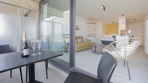 Un salon moderne avec une cloison en verre, une table à manger agrémentée d’une bouteille de champagne et un fauteuil en osier.