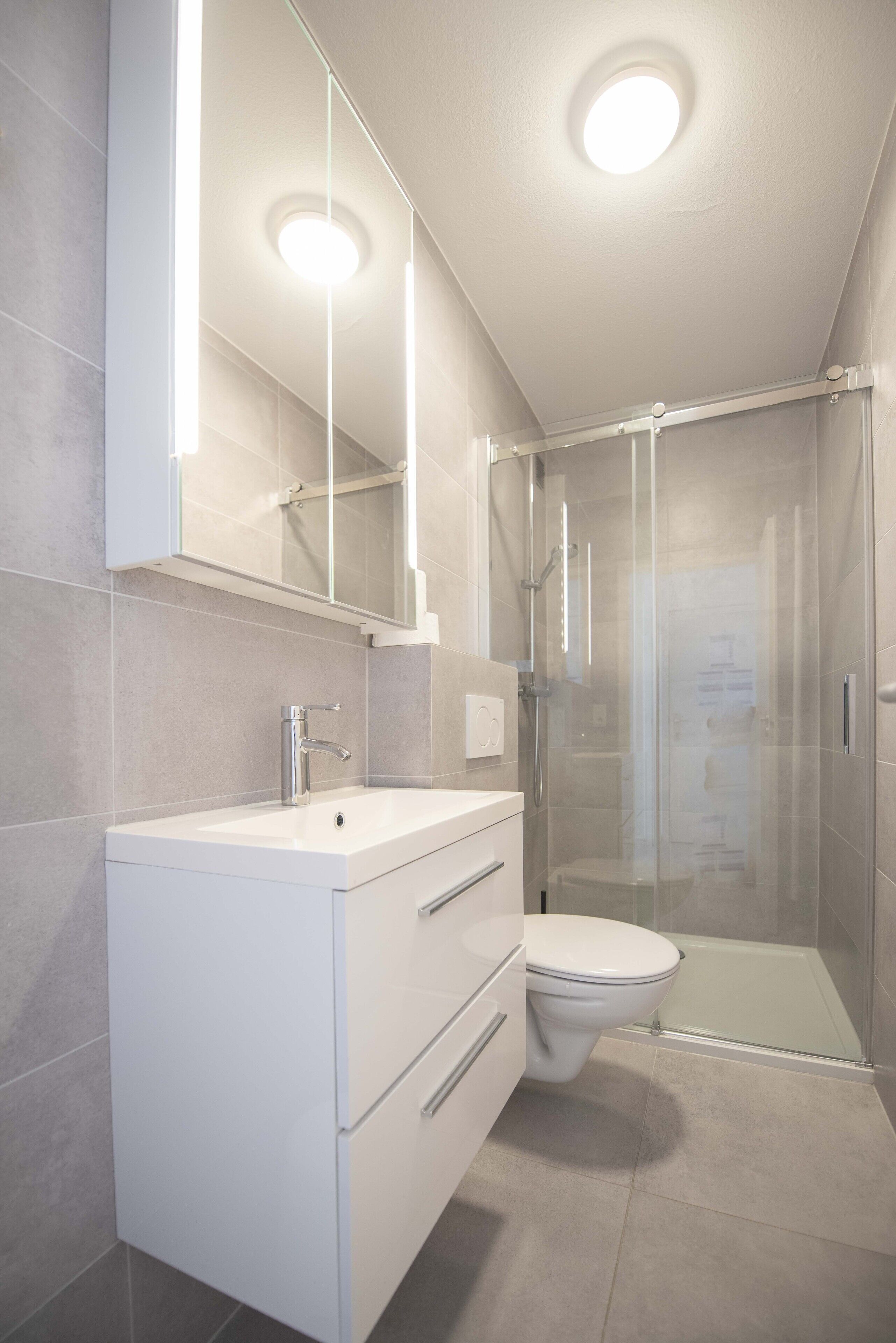 Un baño moderno con cabina de ducha de vidrio, tocador blanco con espejo y retrete.