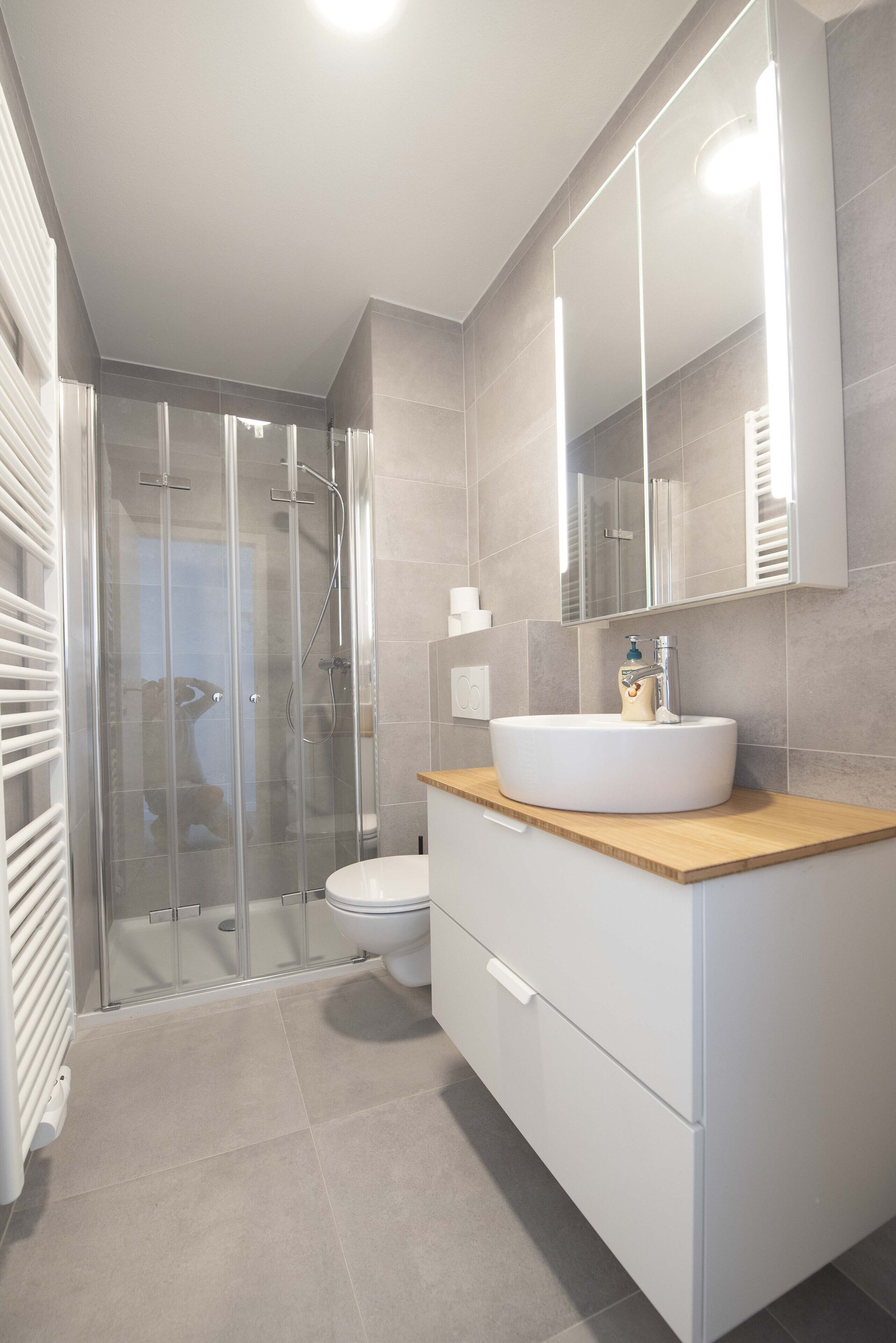 A modern bathroom with a glass-enclosed shower, a white sink, and a large mirror.