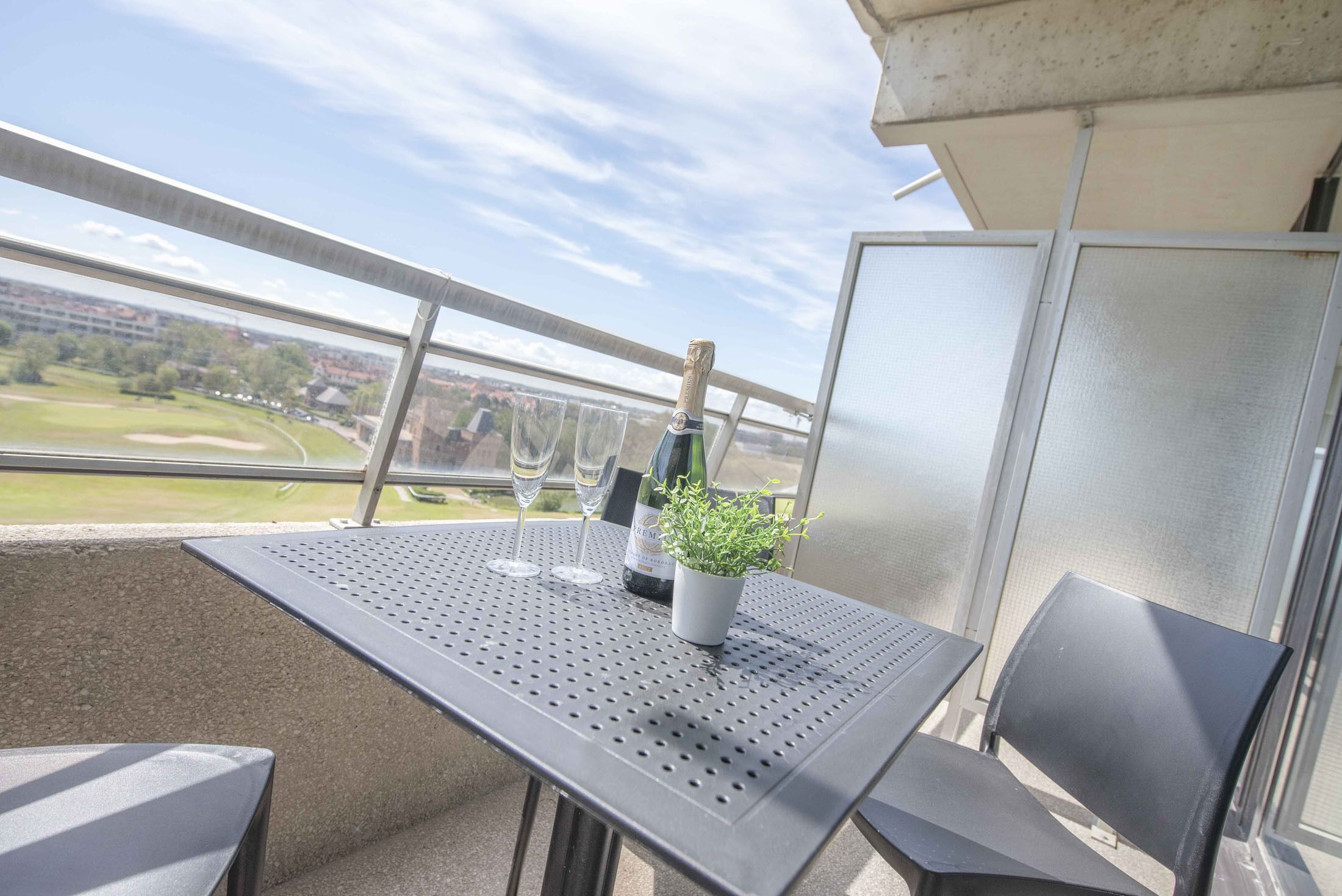 Un balcon avec une table, deux chaises, une bouteille de champagne et une petite plante.