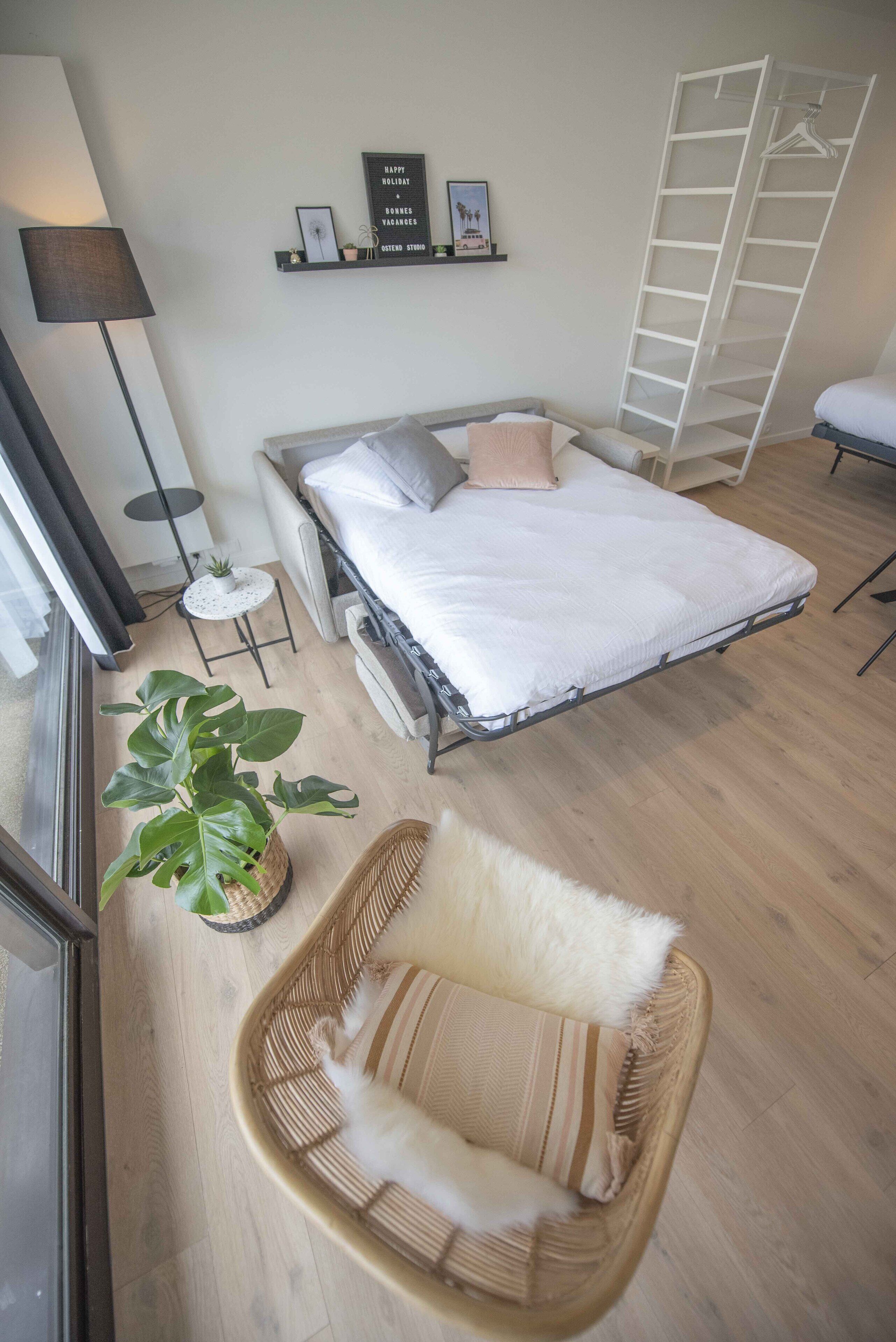 A bedroom with a bed, a bedside table, a lamp, a potted plant, a chair, and a ladder.