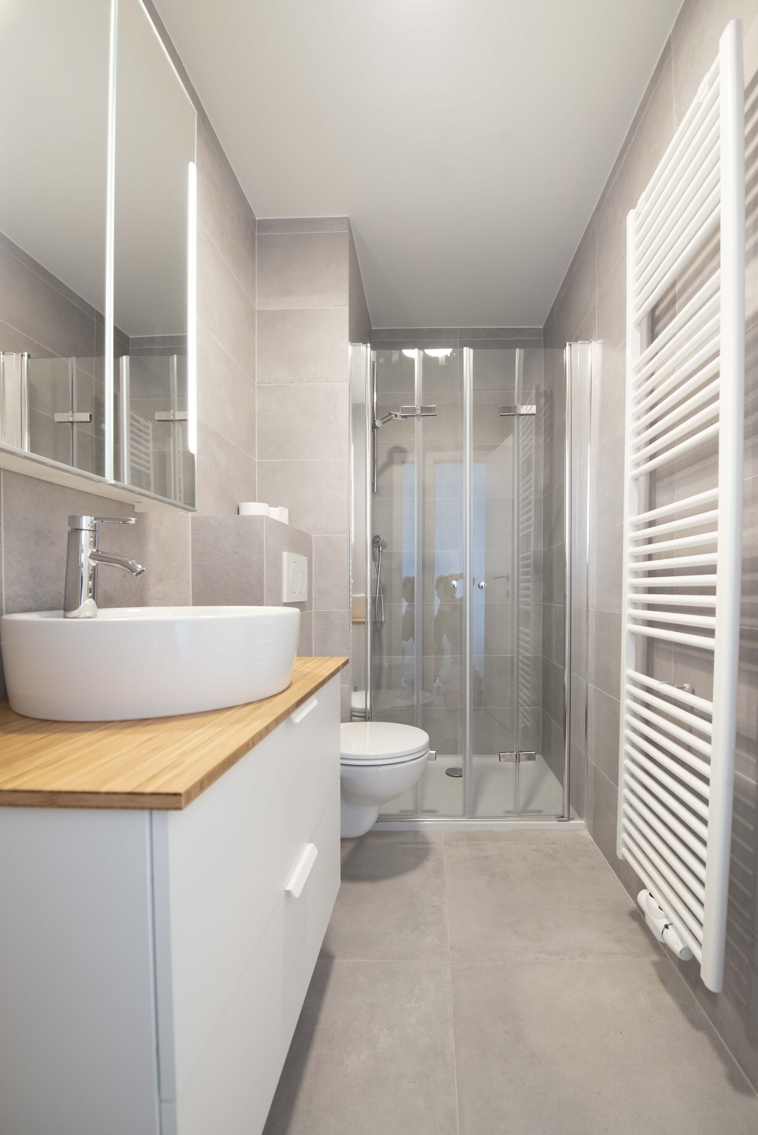 Un baño moderno con un lavamanos grande de color blanco, un espejo, cabina de ducha y un inodoro blanco.