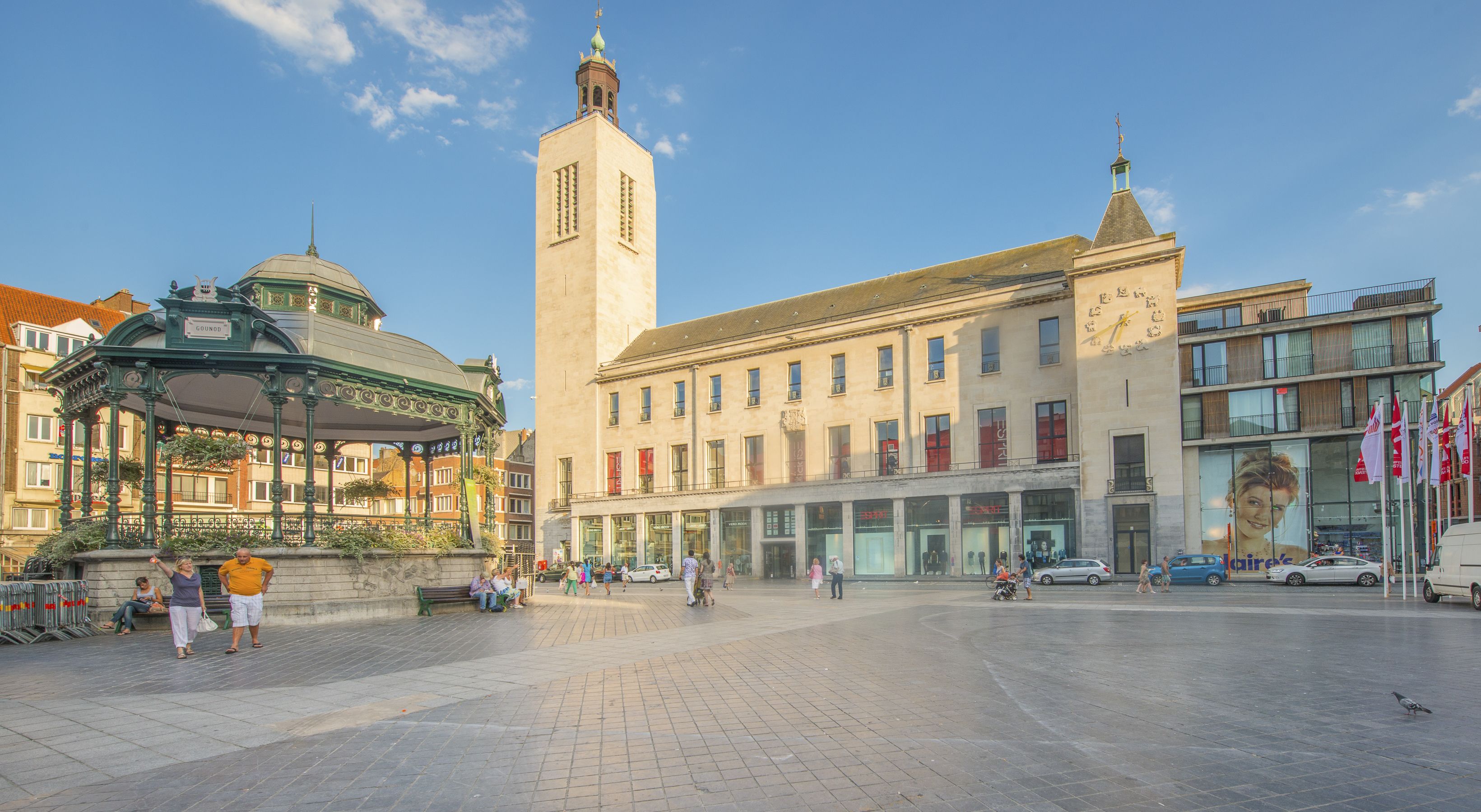 Une place publique abritant un bâtiment historique doté d’une tour horloge et d’un pavillon couvert.