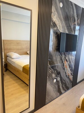 A modern hotel room with a wooden bed, a large mirror, a marble accent wall, and a flat-screen TV mounted on the wall. - Guven Suit Otel (Istanbul)