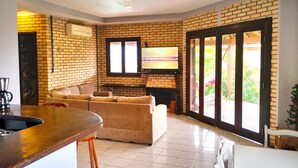 Een moderne woonkamer met een bakstenen muur, een open haard, een televisie en een grote schuifdeur die leidt naar een buitenruimte.