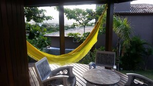 Een houten terras met een gele hangmat, twee stoelen en een tafel.