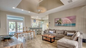 A spacious living area with a sofa, coffee table, and dining table. There is a large window and a painting on the wall. - Coastal Heaven: Huge Lanai-Heated Pool-Canal w Private Dock-River Views (Cape Coral)