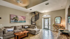 A spacious living room with a large sectional sofa, a wooden coffee table, and a spiral staircase leading to a balcony. - Coastal Heaven: Huge Lanai-Heated Pool-Canal w Private Dock-River Views (Cape Coral)