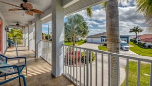 A covered porch with ceiling fans, a view of a residential area with palm trees and a house. - Coastal Heaven: Huge Lanai-Heated Pool-Canal w Private Dock-River Views (Cape Coral)