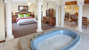 A bedroom with a large bed, a wooden dresser, a mirror, and a blue bathtub.