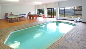 An indoor swimming pool with a view of the outdoors, a pool table, and a foosball table.