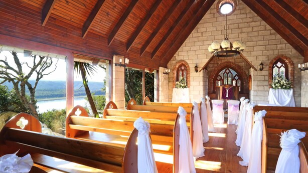 A church interior with wooden pews, a brick altar, and a view of the outdoors.