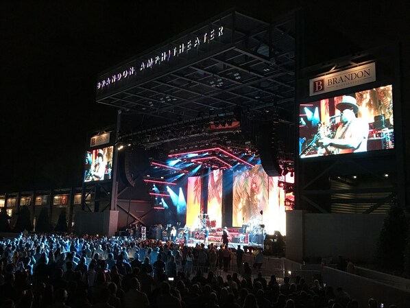 Um palco de concerto ao ar livre grande, com uma multidão de pessoas em primeiro plano.