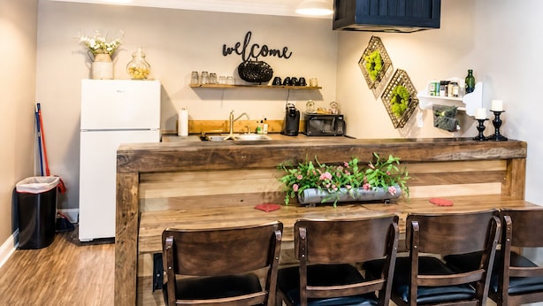 A modern kitchen with a wooden island, a white refrigerator, and a 'welcome' sign on the wall. - The Cottage on College - Pets & Parking (Brandon)