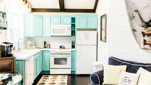 A compact kitchen with teal cabinets, white appliances, and a dining area with a table and chairs.