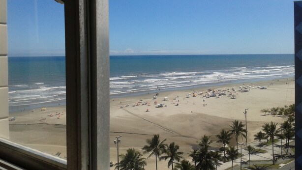 Blick auf einen Strand durch ein Fenster, mit Palmen und Sonnenschirmen.