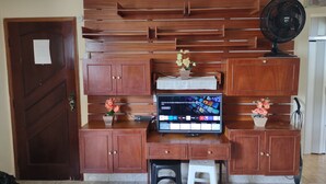 Ein Holzschrank mit einem Flachbildfernseher darauf, einem Ventilator und einer kleinen Pflanze.