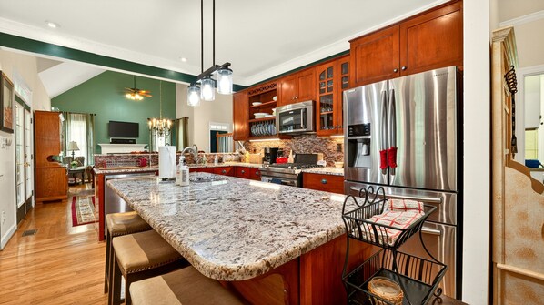 Una cocina con encimeras de granito, electrodomésticos de acero inoxidable, armarios de madera y una isla grande con asientos.