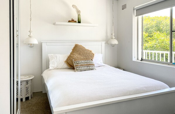 Une chambre à coucher bien rangée, avec un lit, une petite table de chevet et une fenêtre donnant sur un paysage verdoyant.