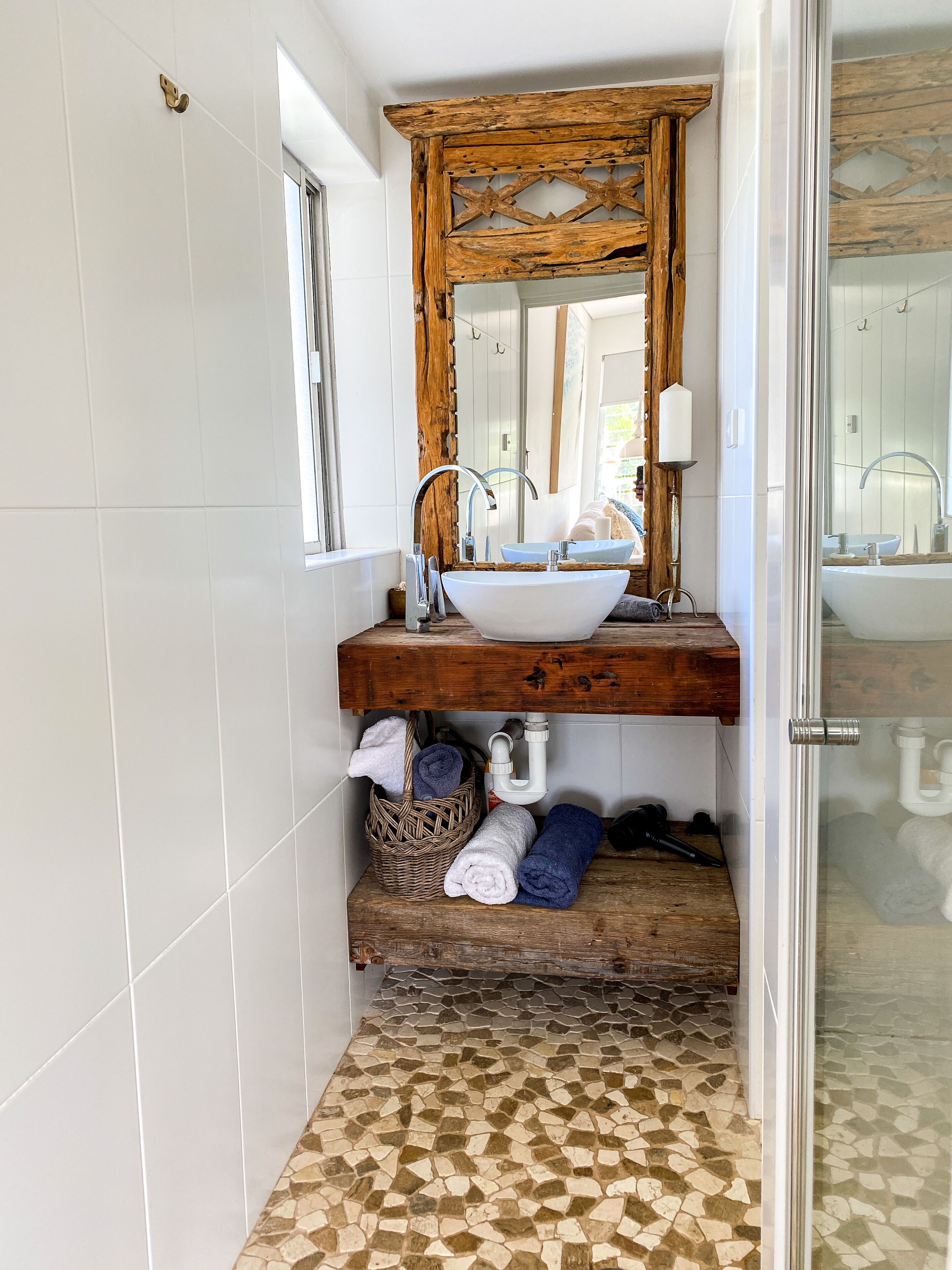 Ein Badezimmer mit einem weißen Waschbecken, einem Holz-Waschtisch und einem Mosaikboden.