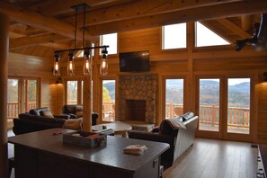 A wooden cabin interior with a stone fireplace, leather furniture, and a large window overlooking a mountainous landscape. - Private Log Cabin with an AMAZING VIREW!!!  Hot Tub and Sleeps up to 14 (Gilead)