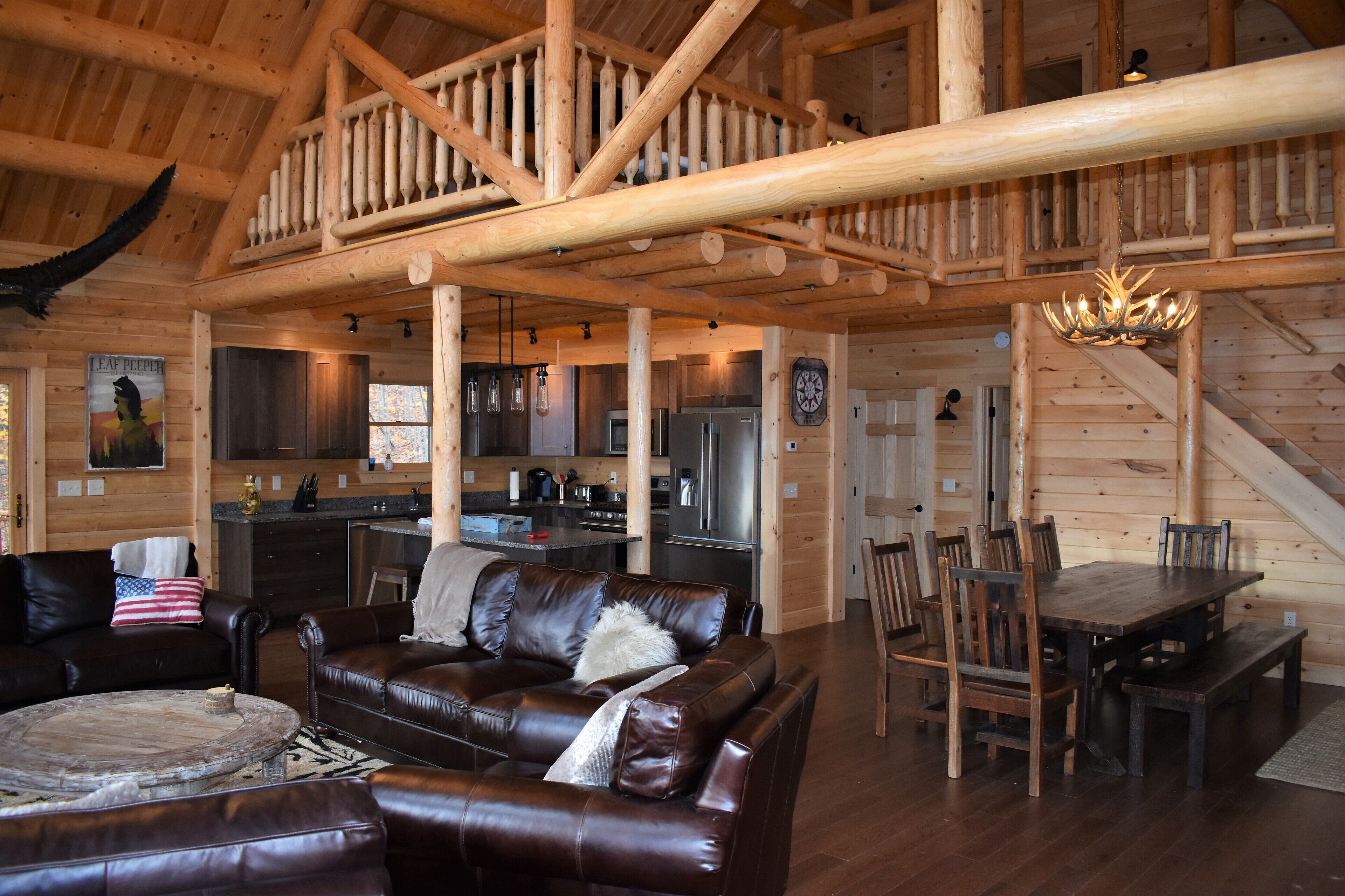 Un intérieur spacieux de chalet en bois, comprenant un salon, un coin repas, une cuisine et un escalier.