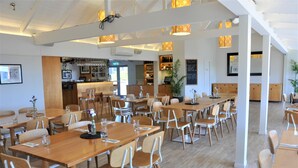 Un'ampia sala da pranzo con tavoli e sedie in legno, un'area bar con scaffali pieni di bottiglie e una grande pianta in vaso.