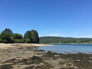 A beach with rocky shoreline, trees, and a distant hill with houses. - Ocean view home with private beach. (Bar Harbor)