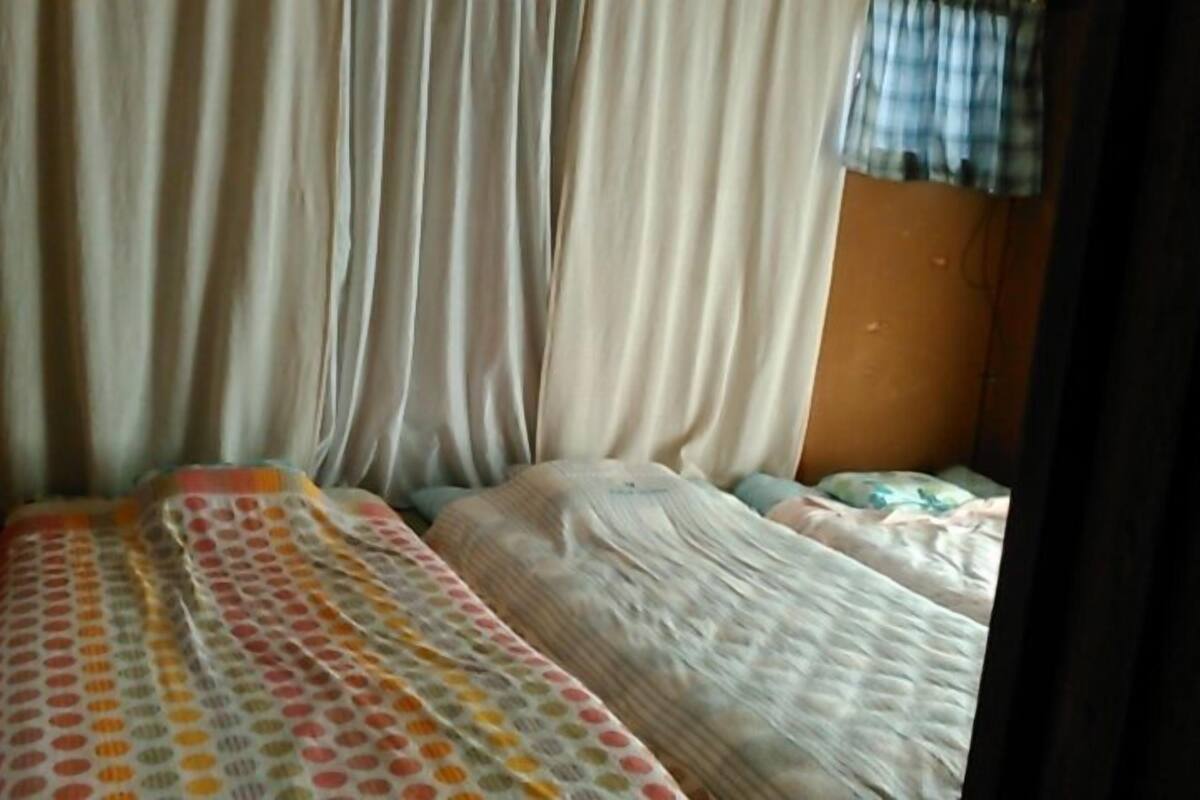 Habitación con dos camas, cada una con una colcha de estampado diferente. Tiene una cortina en un lateral y una ventana con cortina a cuadros.
