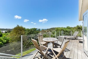 En træterrasse med et rundt bord og stole, med udsigt over et naturskønt landskab.