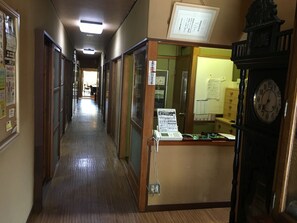 A hallway with wooden floors, a reception desk, a clock, and various notices on the walls.