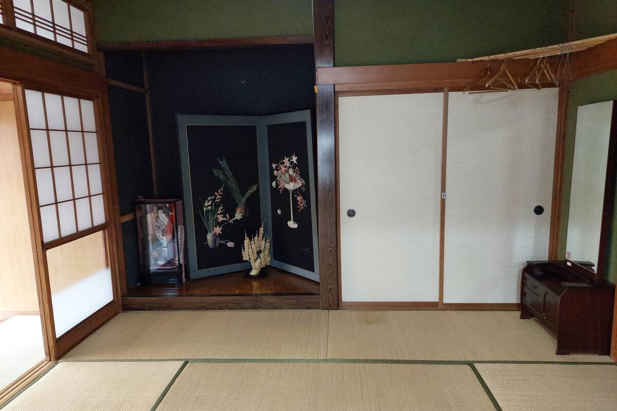A traditional Japanese room with tatami flooring, shoji screens, a sliding door, and a small cabinet.