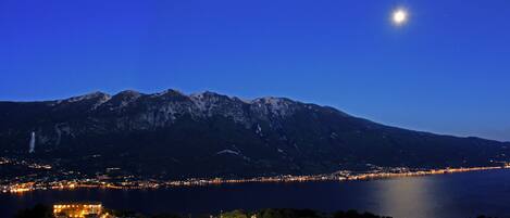 A mountain range at dusk with a lake in the foreground and a town along the shoreline.
