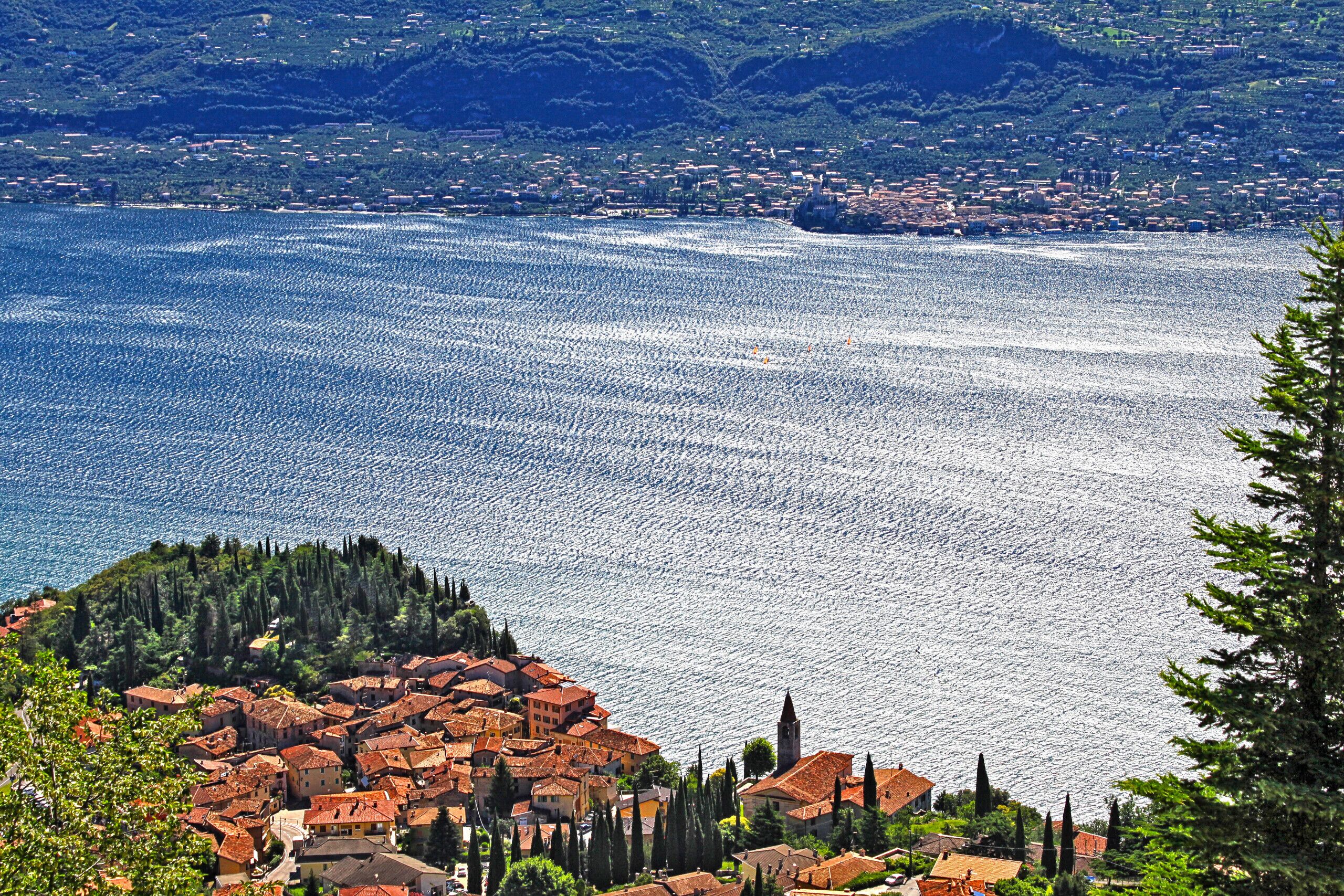 A coastal town with terracotta-roofed buildings, a clear view of the sea, and a backdrop of green hills.