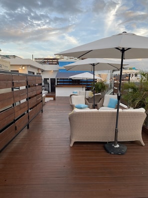 A wooden deck with outdoor seating, including a wicker sofa and chairs, under large umbrellas. - 352 Guest House (San Juan)