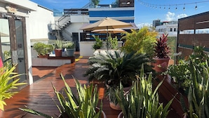A rooftop terrace with potted plants, a wooden deck, and a blue and white building in the background. - 352 Guest House (San Juan)