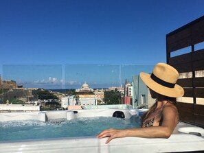 Una persona relajándose en un jacuzzi con vistas a un paisaje urbano y un edificio grande con cúpula.