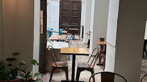 An outdoor café with tables and chairs, potted plants, and a wooden door in the background.