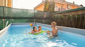 Une piscine entourée d’un filet, un enfant sur un flotteur et une personne en maillot de bain.