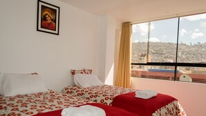 A hotel room with two beds, a large window with a city view, and a framed picture on the wall. - Mayte Apartment (Cusco)