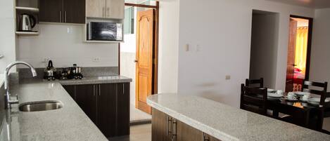 A modern kitchen with granite countertops, dark wooden cabinets, a stainless steel sink, and a built-in microwave.
