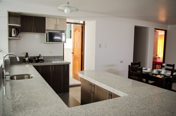 A modern kitchen with granite countertops, dark wooden cabinets, a stainless steel sink, and a built-in microwave.