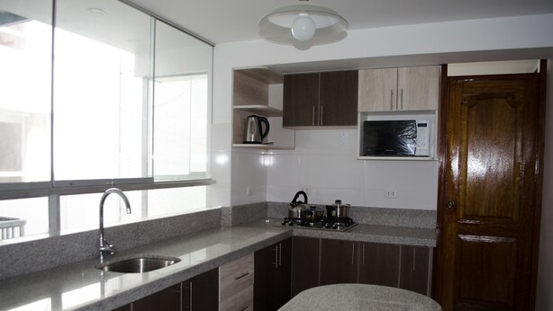 A kitchen with a sink, stove, microwave, and cabinets. - Mayte Apartment (Cusco)
